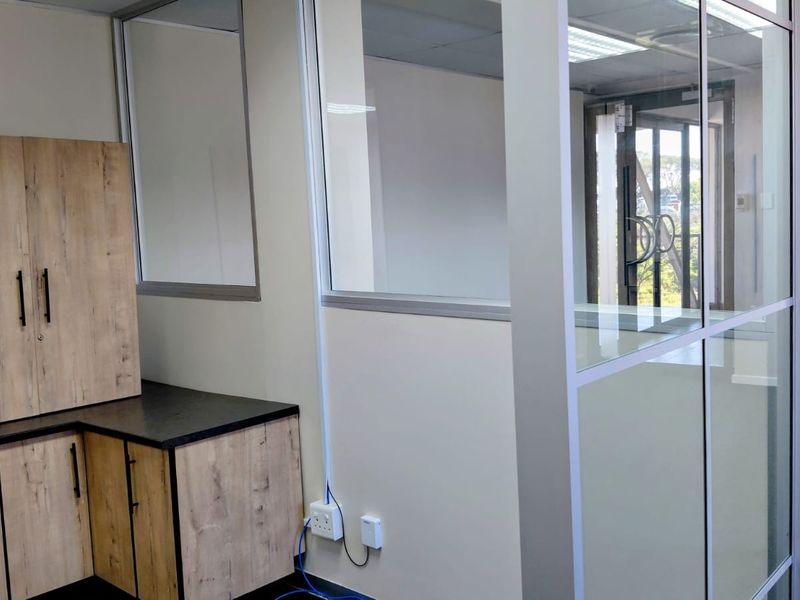 A modern office space featuring glass partition walls, built-in wood-finish cabinetry, and clean carpet flooring, providing a professional and bright work environment.