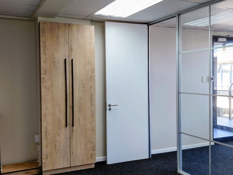 A modern office space featuring built-in wood-finish cabinetry, a glass partition wall, and professional carpet flooring with recessed ceiling lighting.
