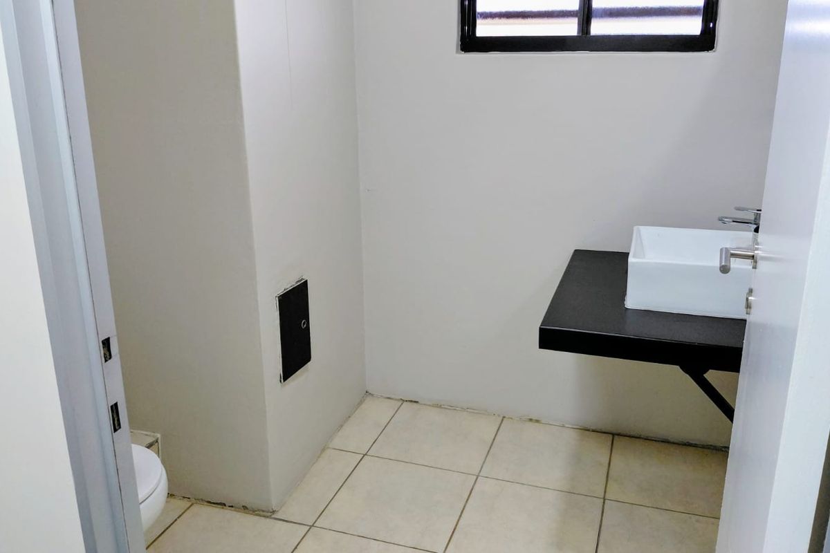 A compact office bathroom featuring a modern vessel sink on a black vanity countertop, tiled flooring, and a window for natural light.