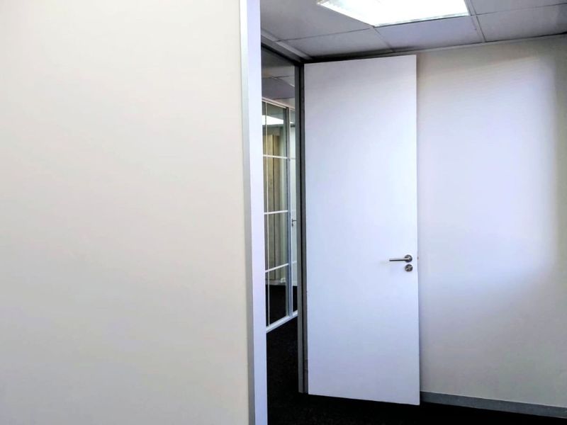 A clean, empty office space featuring a suspended ceiling, recessed lighting, and a glass partition, providing a professional and versatile work environment.