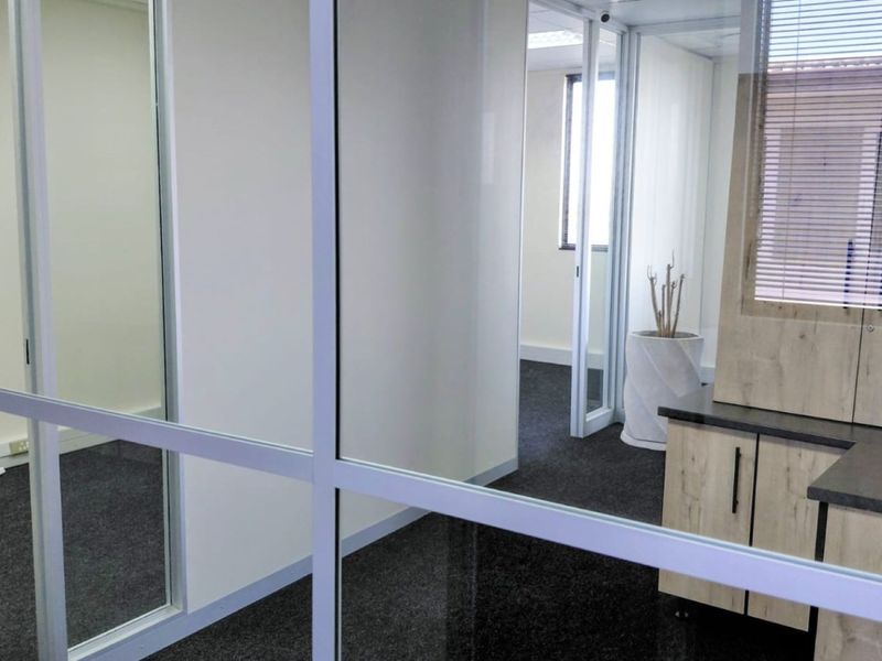 Modern office space featuring glass partitioning, built-in cabinetry, and dark carpeting, offering a clean and professional environment.