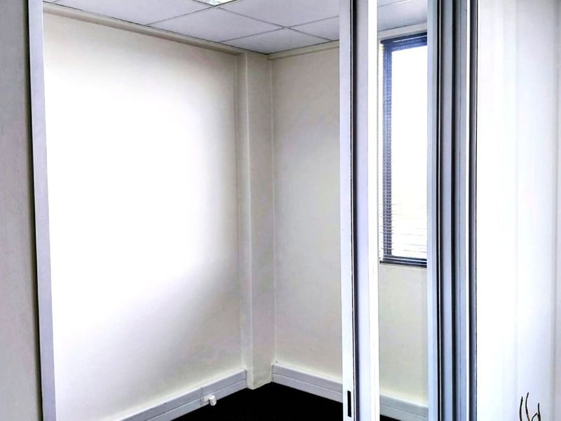 A vacant office space featuring a suspended ceiling, sliding door access, and a window with fitted blinds.