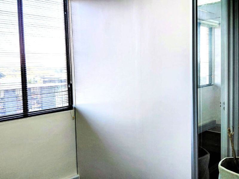 A bright, empty office space featuring large windows with venetian blinds and a modern glass partition wall.