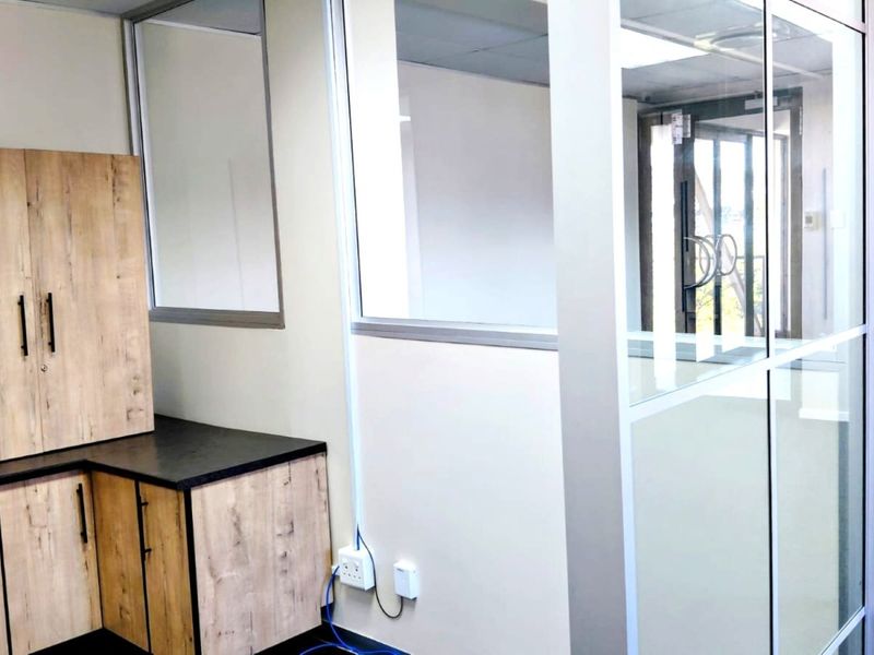 A modern, empty office space featuring glass partitions, built-in wood-finish cabinetry, and clean, neutral finishes, ideal for a professional workspace.