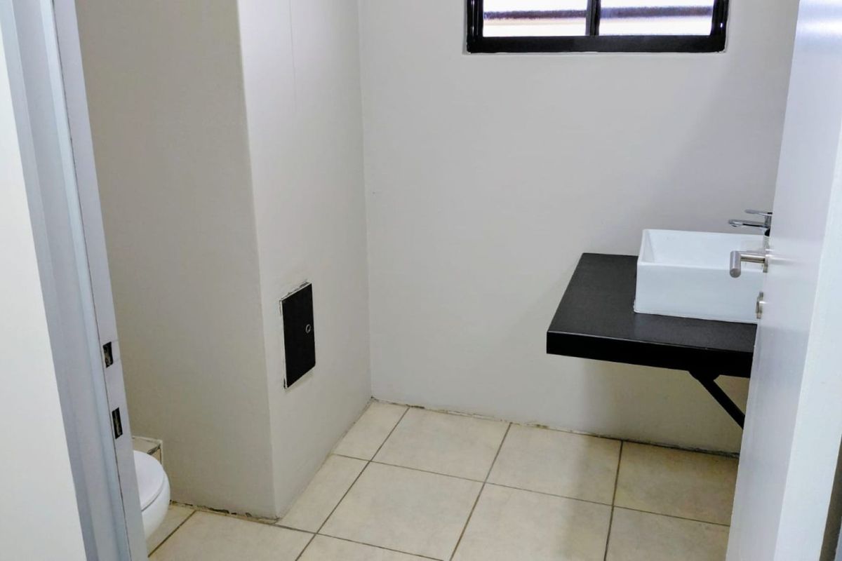 A compact, minimalist bathroom featuring a floating vanity shelf with a modern basin, ceramic floor tiles, and a window for natural light.