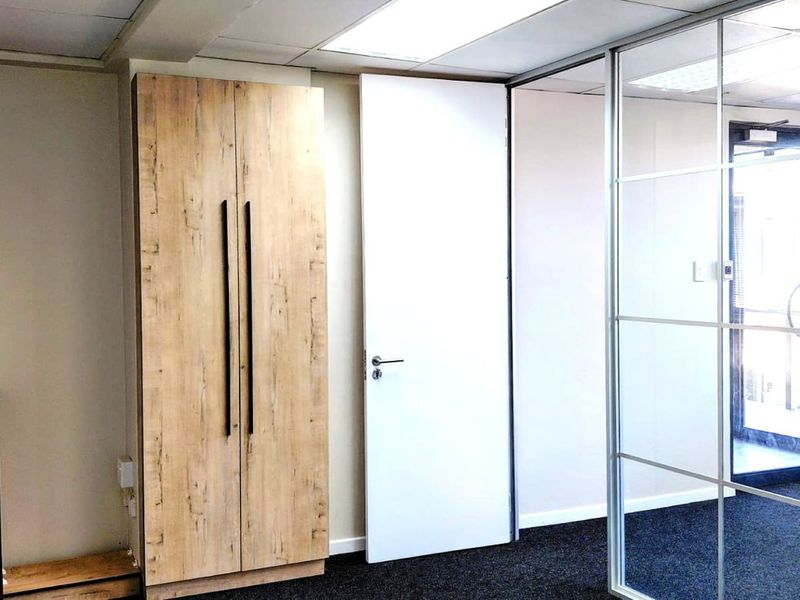 A modern office space featuring built-in wood-finish cabinetry, a glass partition wall, and clean carpet flooring.