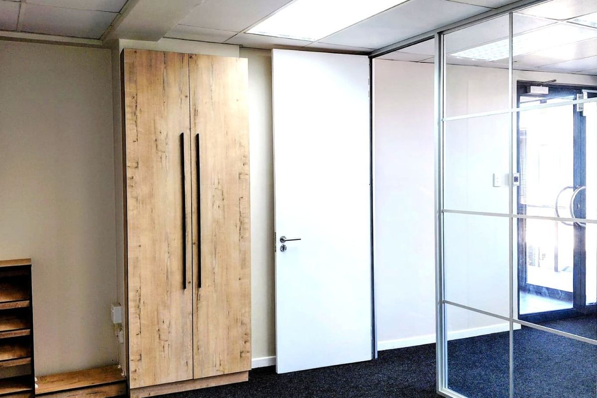 A modern office space featuring built-in wood-finish cabinetry, a glass partition wall, and clean carpet flooring.