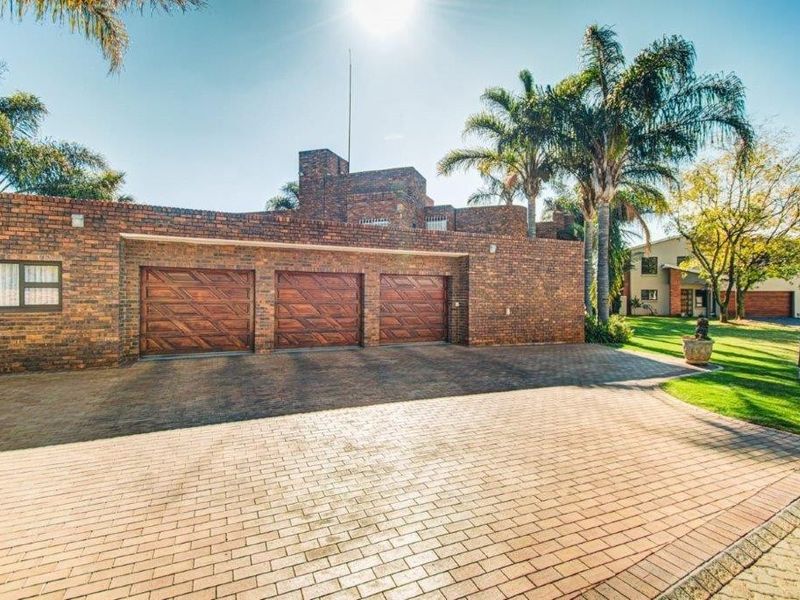 A well-maintained front exterior featuring a triple garage with wooden doors, a spacious paved driveway, and established garden landscaping.