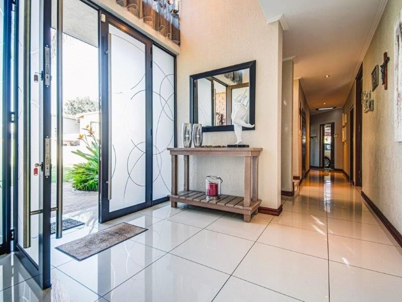Bright and welcoming entrance hall featuring large glass panelled doors, polished tiled flooring, and recessed downlighting leading into the home's interior.