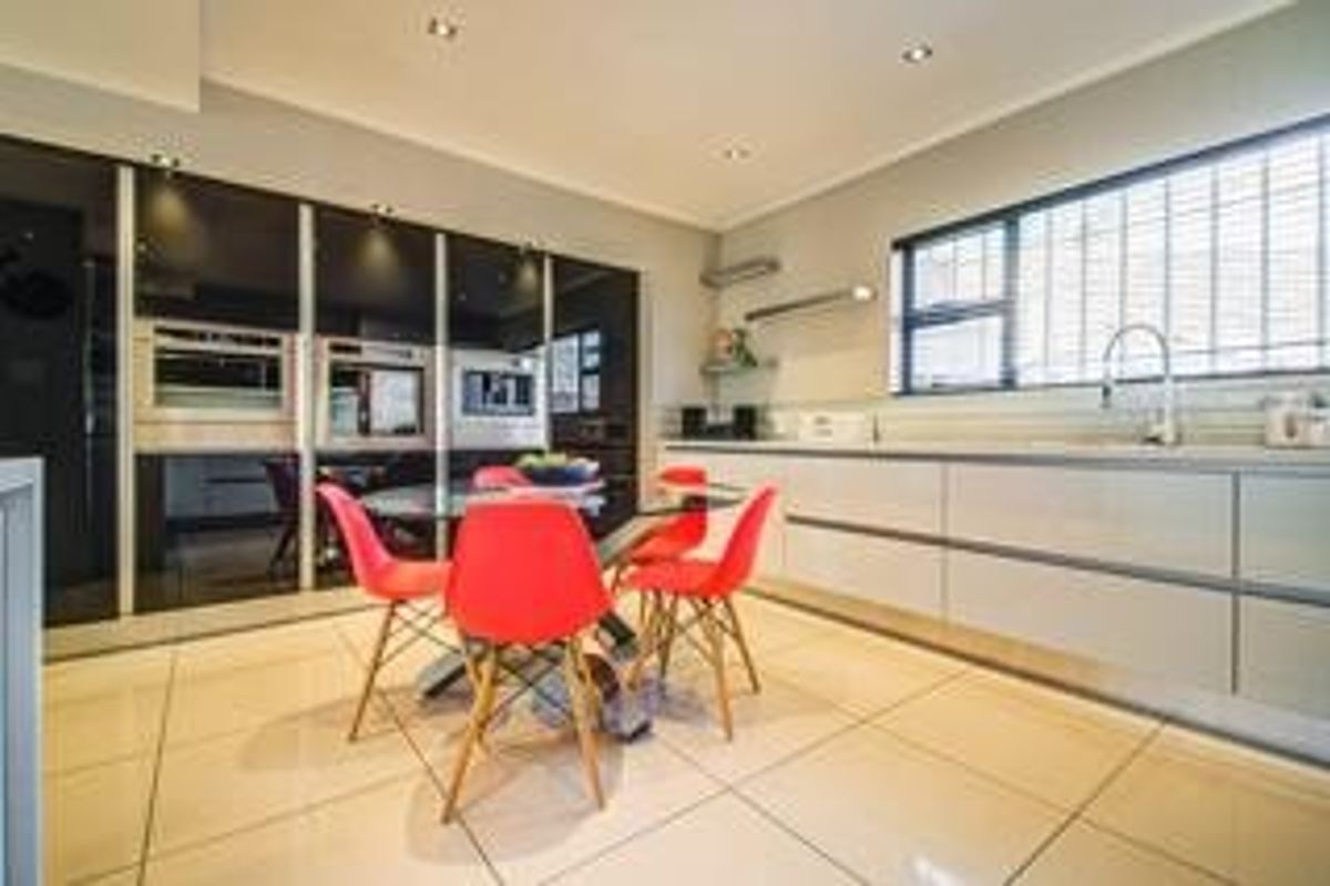 Modern kitchen featuring sleek integrated cabinetry, built-in appliances, tiled flooring, and ample natural light through a large window with security bars.