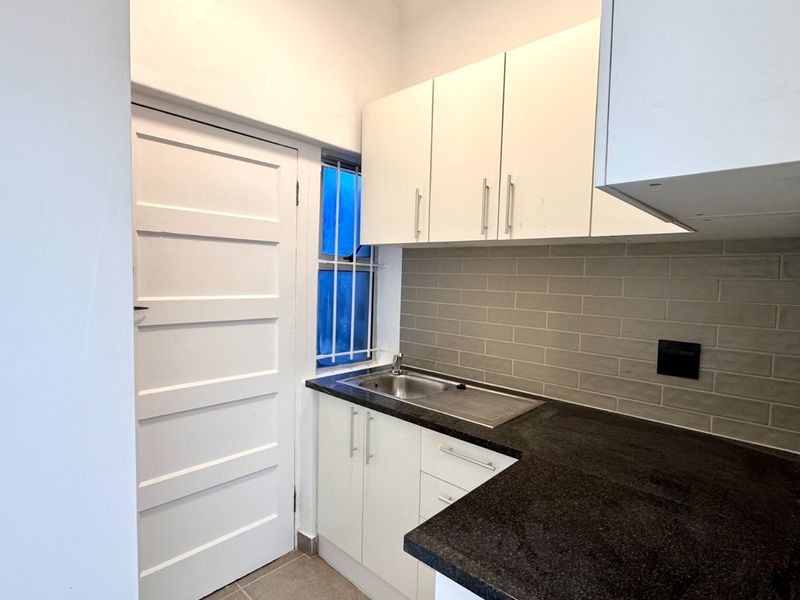 A compact, modern kitchen featuring white cabinetry, dark stone countertops, and a grey subway tile backsplash with a functional sink area.