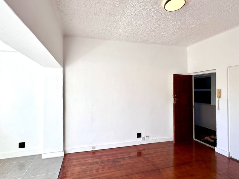 An empty living area featuring a combination of hardwood and tiled flooring, a built-in cupboard, and an intercom system.
