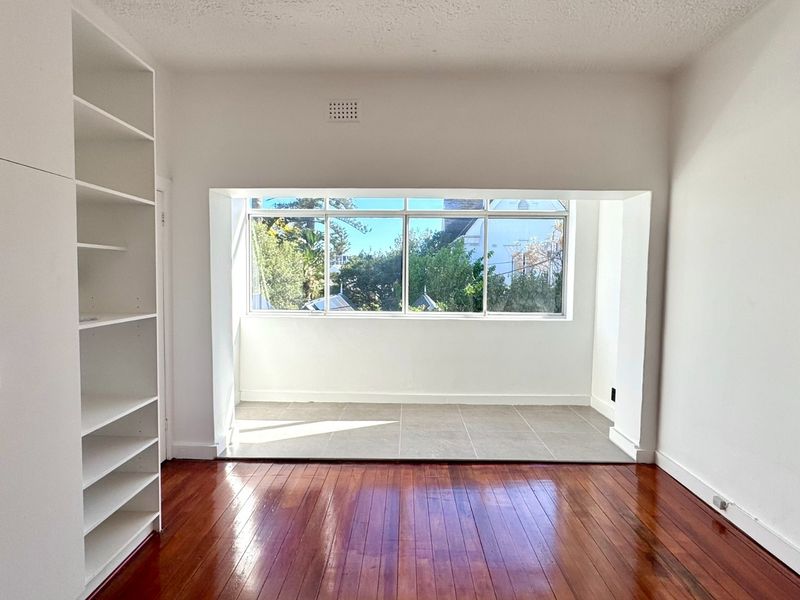 Bright bedroom featuring polished timber flooring, built-in storage cabinetry, and an adjoining tiled sunroom area with large windows providing natural light.