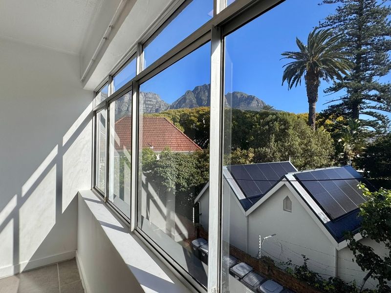 A bright, enclosed balcony featuring large aluminum-framed windows that offer scenic mountain and neighborhood views.