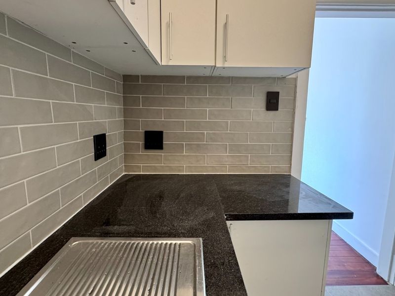 A compact kitchen area featuring a dark granite countertop, stainless steel sink, subway tile backsplash, and white cabinetry.