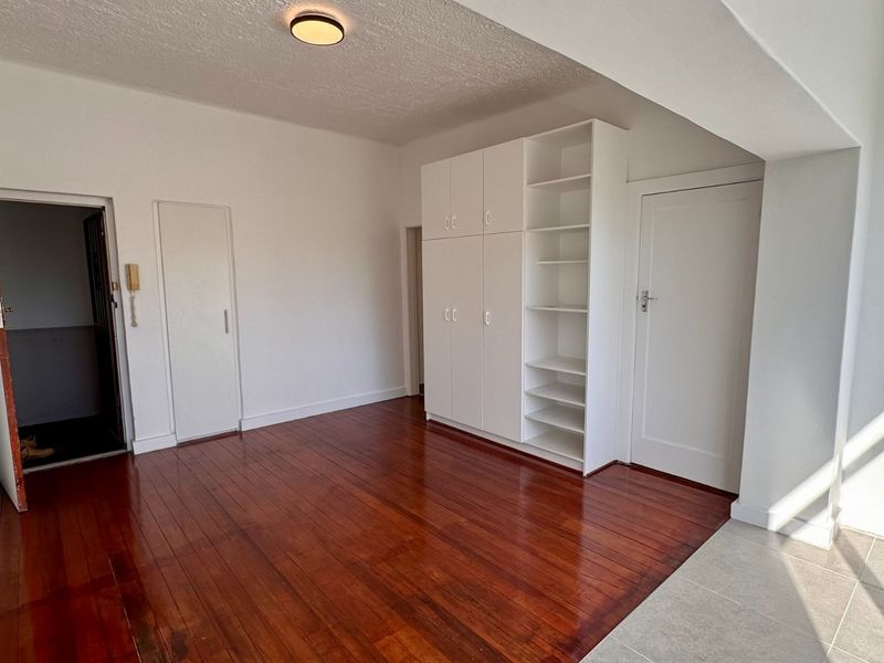 An empty living area featuring polished hardwood floors, built-in storage cabinetry, and a neutral color palette, offering a versatile space for customization.
