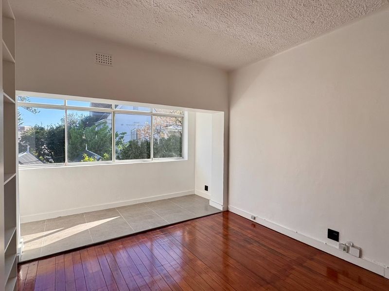 A bright, empty bedroom featuring polished timber flooring, a tiled alcove area, and built-in storage cabinetry.