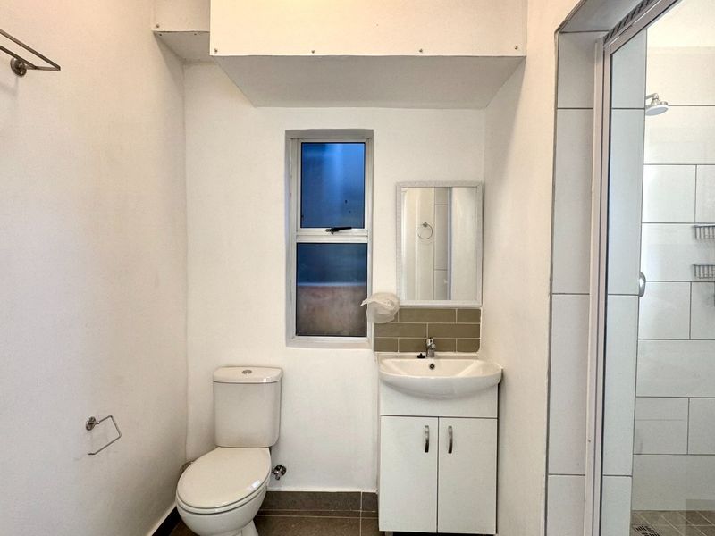 A functional bathroom featuring a white vanity, toilet, and a separate shower enclosure with tiled walls.