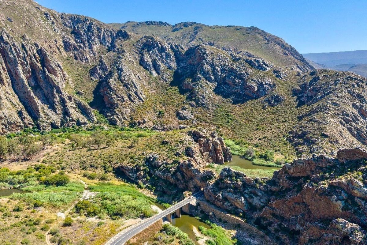 An aerial view of the farm landscape featuring a bridge crossing a river nestled within a dramatic mountain pass.