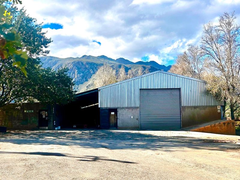 Large industrial-style farm shed featuring corrugated metal cladding, a roller shutter door, and a covered loading area set against a mountain backdrop.
