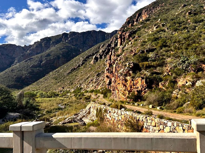 A scenic view of a rugged mountain landscape featuring a stone retaining wall and a concrete bridge railing in the foreground.