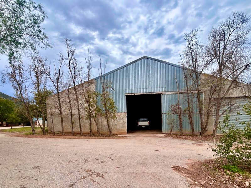 Large agricultural utility shed featuring corrugated metal siding, a wide sliding entrance, and a secondary roller shutter door on a rural farm property.