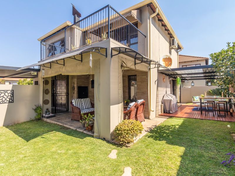 Rear view of the property featuring a covered patio, timber deck, upper balcony with metal railings, and a well-maintained garden area.
