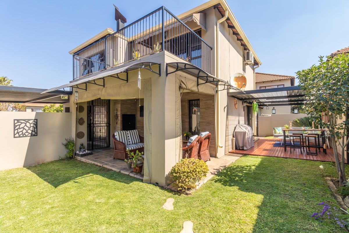 Rear view of the property featuring a covered patio, timber deck, upper balcony with metal railings, and a well-maintained garden area.