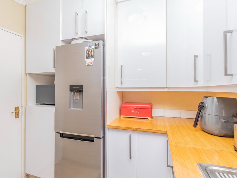 A compact kitchen featuring modern white gloss cabinetry, warm wooden countertops, and a stainless steel sink, providing a clean and functional workspace.