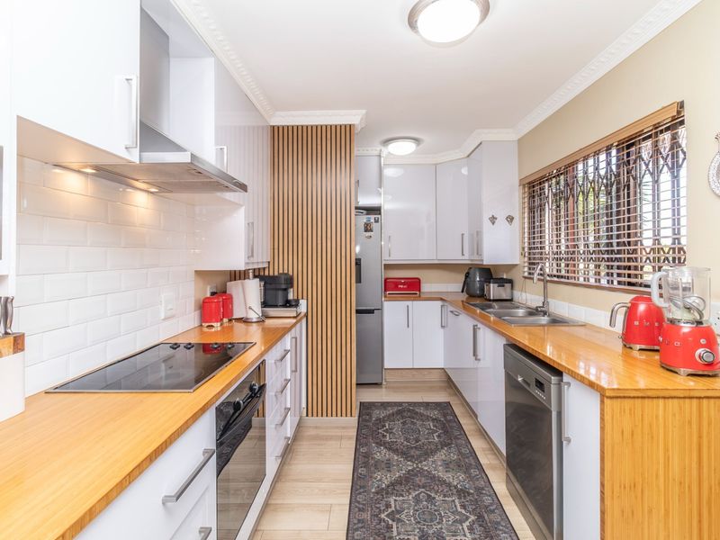 Modern galley-style kitchen featuring white gloss cabinetry, warm wooden countertops, subway tile backsplash, and a stylish slatted wood feature wall.