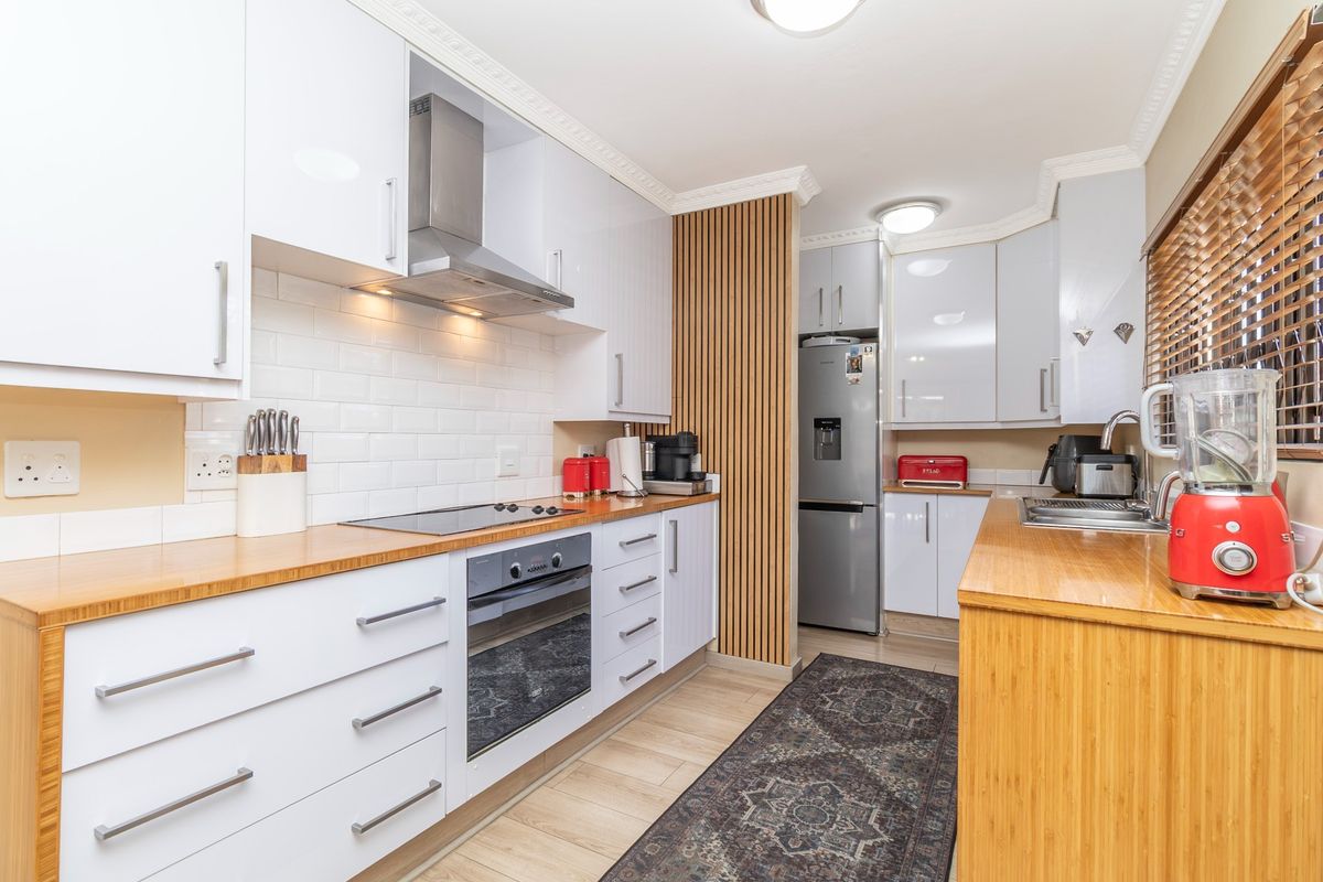 Modern kitchen featuring white cabinetry, wooden countertops, subway tile backsplash, and a stylish slatted wood feature wall with integrated appliances.