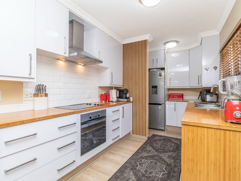 Modern kitchen featuring white cabinetry, wooden countertops, subway tile backsplash, and a stylish slatted wood feature wall with integrated appliances.