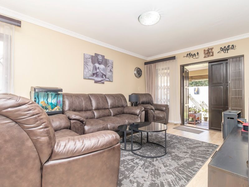 A comfortable living room featuring laminate flooring, decorative cornicing, and direct access to an outdoor patio area through a sliding door.