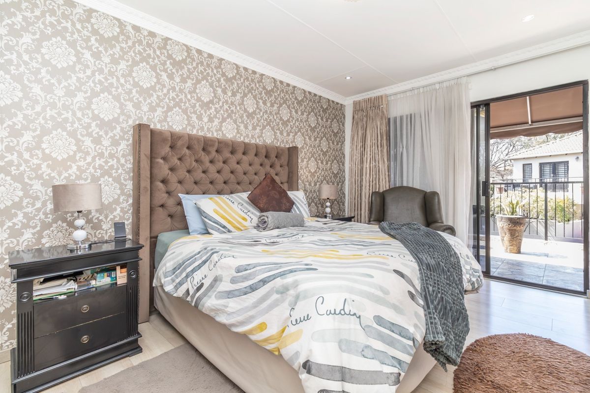 A well-maintained bedroom featuring patterned wallpaper, crown molding, and direct access to a private balcony through sliding glass doors.