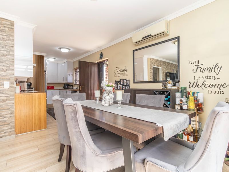 Open-plan dining area featuring timber-look flooring, a stone-cladding accent wall, and integrated air conditioning, flowing seamlessly into the adjacent kitchen space.