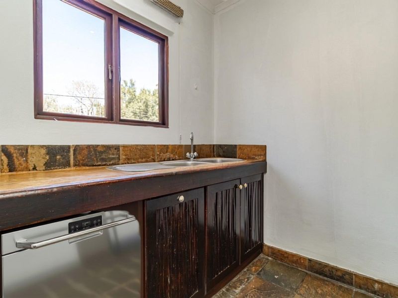 A functional scullery area featuring dark timber cabinetry, a double sink, stone tile backsplash, and stone flooring, offering a practical prep or wash-up space.