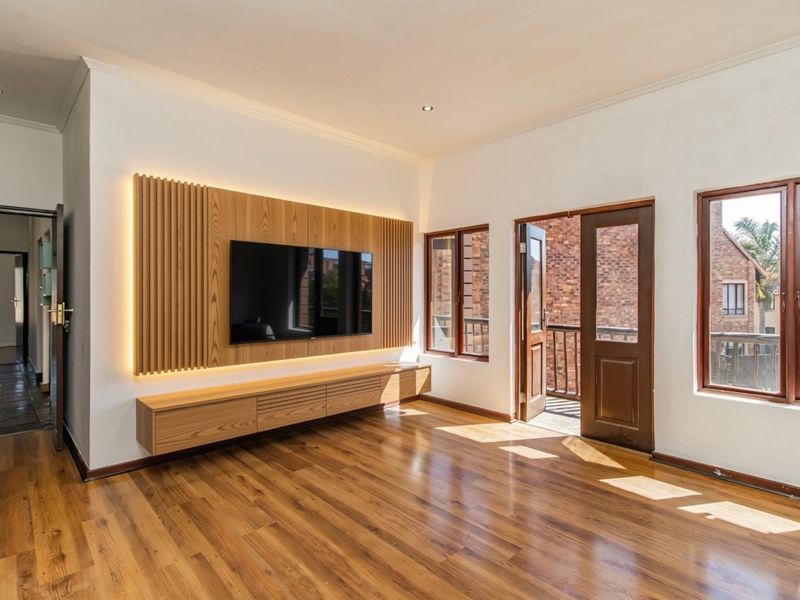 Bright living room featuring high-quality hardwood flooring, a custom slatted wood media wall with integrated lighting, and direct access to a private balcony.