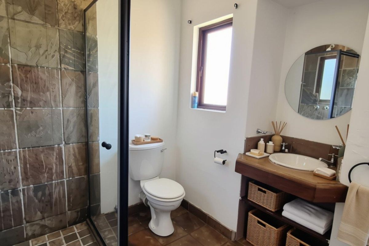 A well-maintained bathroom featuring a walk-in shower with stone tiling, a wooden vanity with integrated basin, and a modern glass shower enclosure.