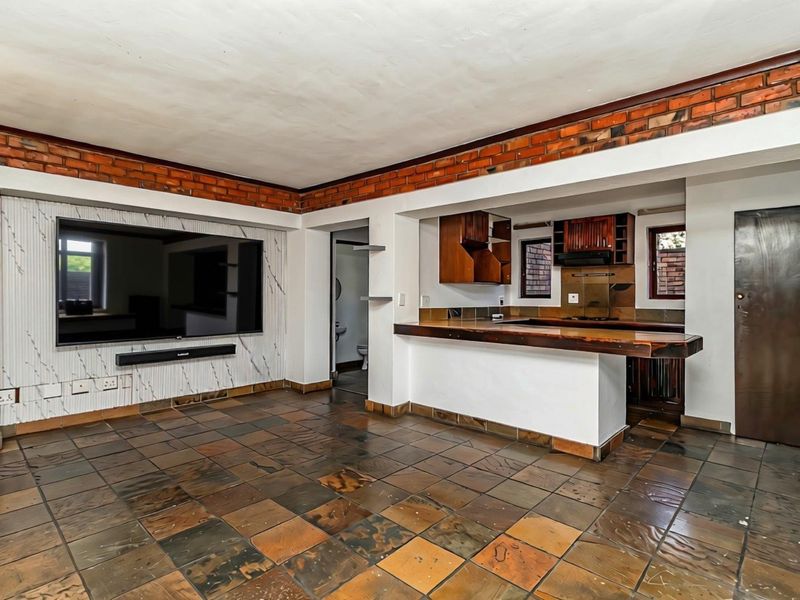 Open-plan living and kitchen area featuring exposed brick accents, slate tile flooring, and a breakfast bar, offering a versatile space for modern living.