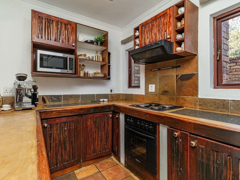 A functional kitchen featuring rustic wooden cabinetry, stone countertops, built-in oven, hob, and extractor fan with a classic tiled splashback.