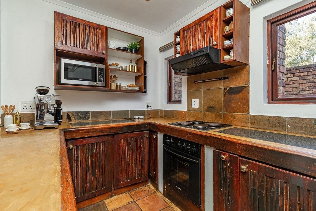 A functional kitchen featuring rustic wooden cabinetry, stone countertops, built-in oven, hob, and extractor fan with a classic tiled splashback.
