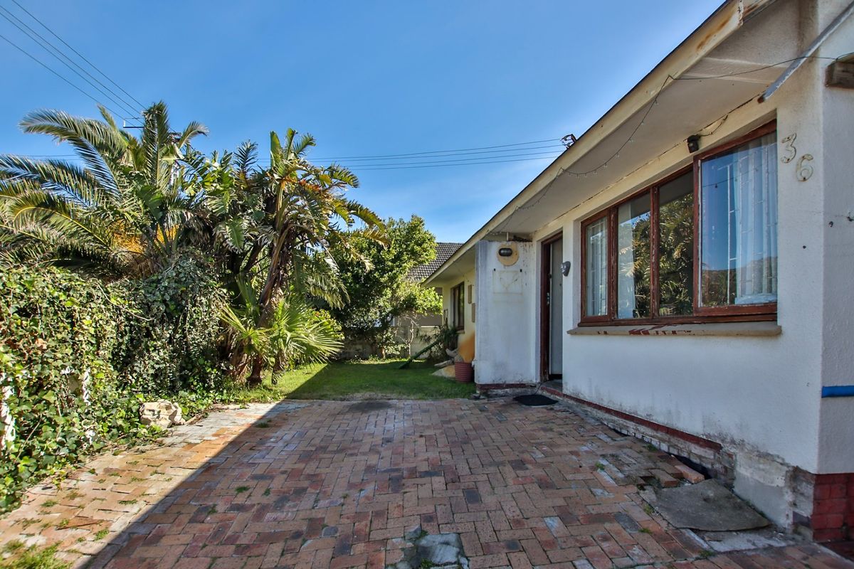 Rear exterior view of the property featuring a brick paved patio area, established garden, and timber-framed windows with security bars.