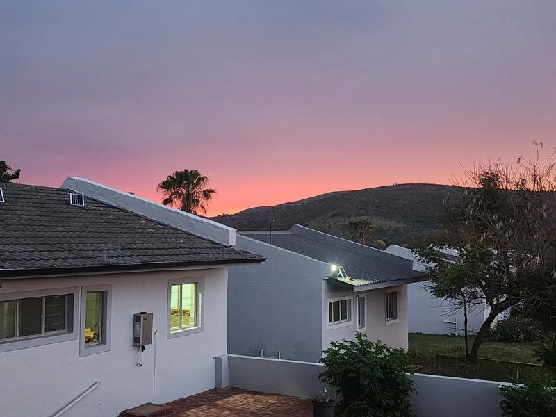 A scenic view of the property exterior at sunset, featuring tiled roofing, a wall-mounted gas geyser, and a paved patio area.