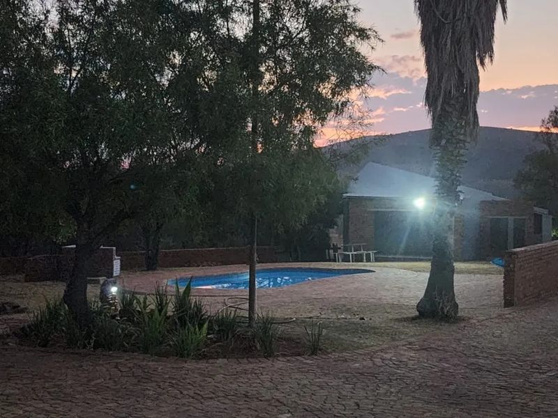 Outdoor pool area featuring a paved patio and brick boundary wall, set against a natural landscape at dusk.