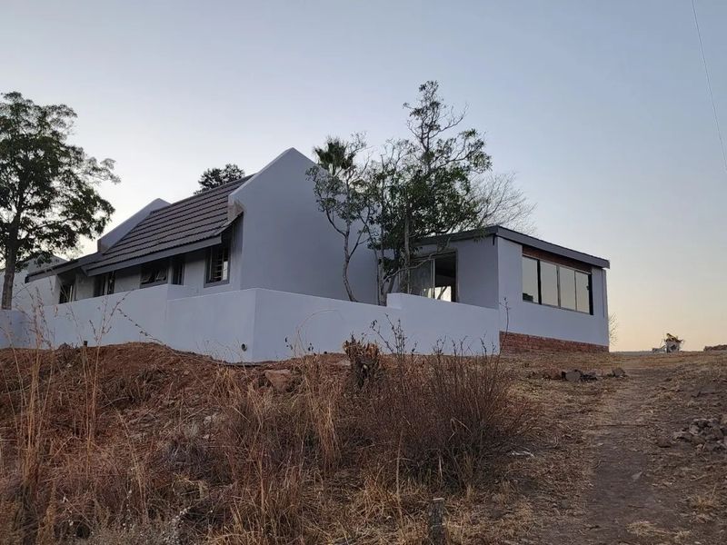 Rear view of a residential property featuring a tiled roof, boundary wall, and large sliding glass doors, set on an undeveloped plot.