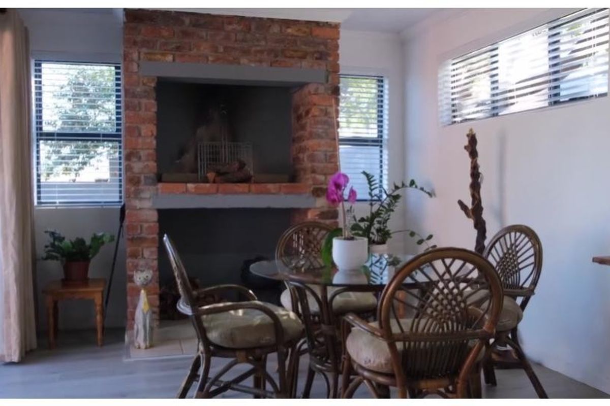 A bright living area featuring a prominent exposed brick fireplace, modern laminate flooring, and large sliding glass doors providing natural light.