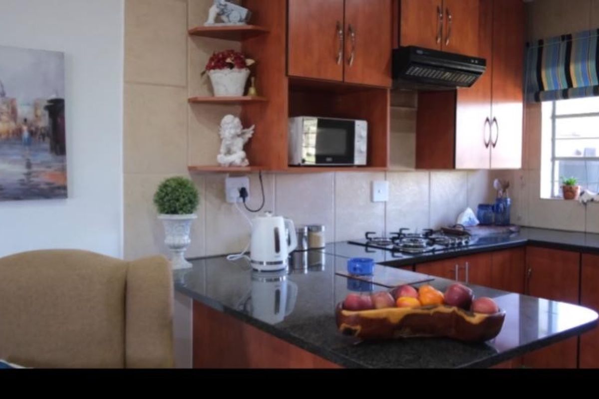 A functional kitchen featuring dark granite countertops, warm-toned wooden cabinetry, a gas hob, and a tiled backsplash.