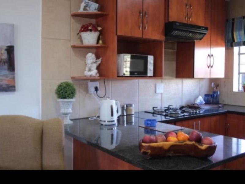 A functional kitchen featuring dark granite countertops, warm-toned wooden cabinetry, a gas hob, and a tiled backsplash.
