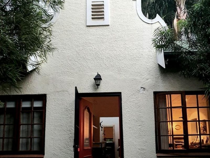 A charming Cape Dutch style rear facade featuring a distinctive curved gable, timber-framed windows, and a welcoming entrance.