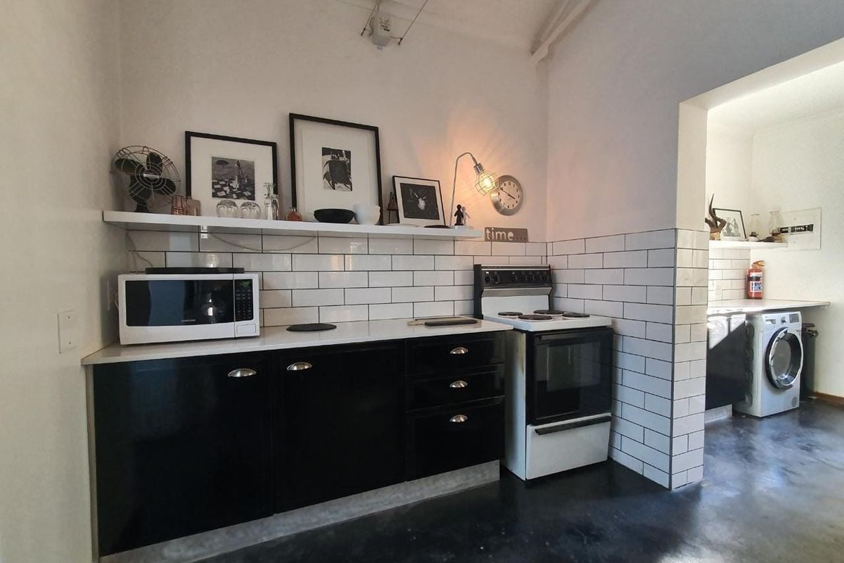 A compact kitchen featuring black cabinetry, white subway tile backsplash, concrete flooring, and a built-in stove, with an adjacent laundry area visible.